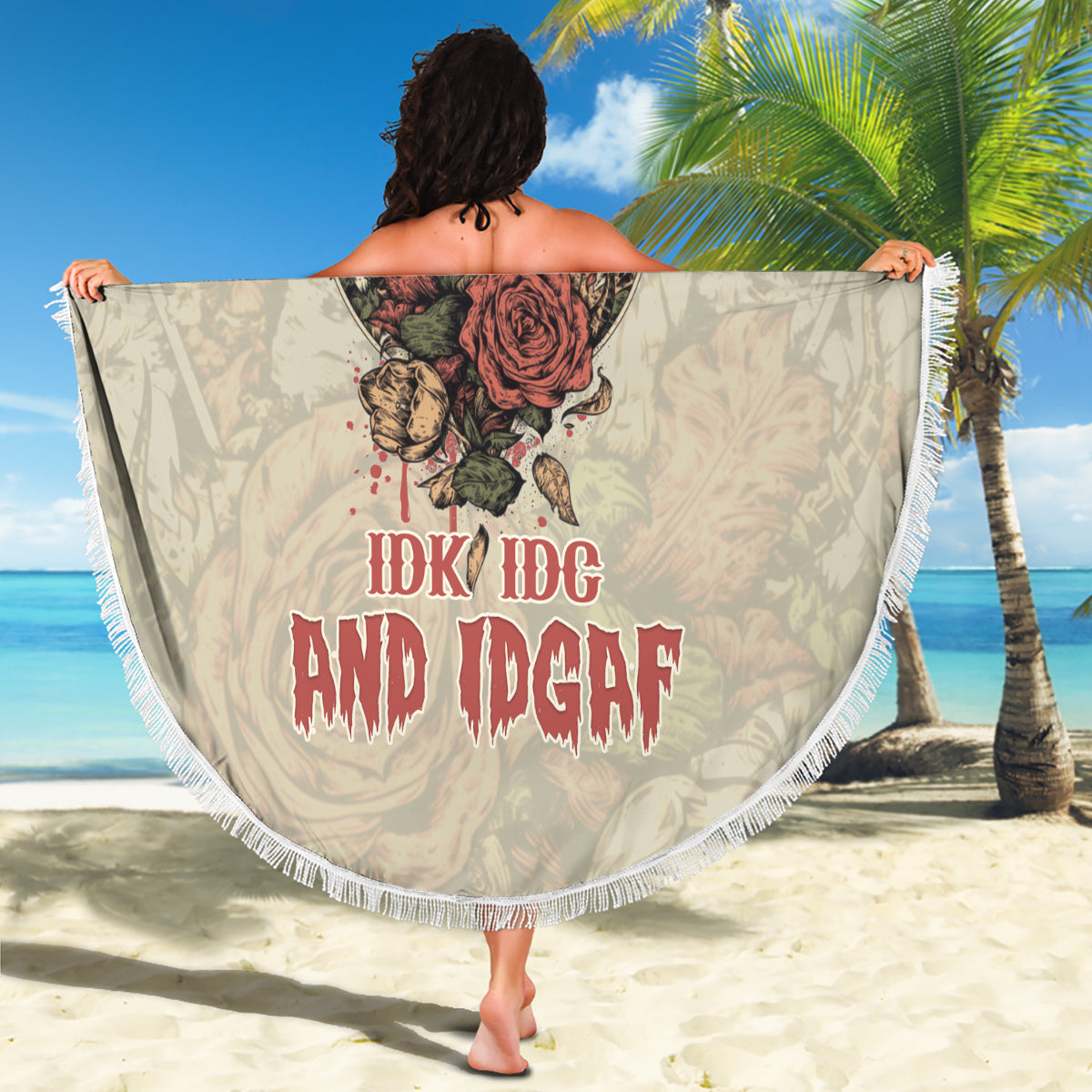 Round beach blanket held flat; skull-and-rose design with red text, white fringe border
