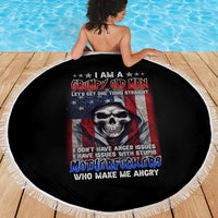 Round black beach blanket with skull-and-flag artwork and white fringe trim, laid on wood