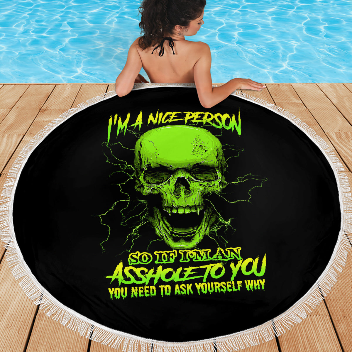Round black beach blanket with neon green skull print and white fringe, spread on deck