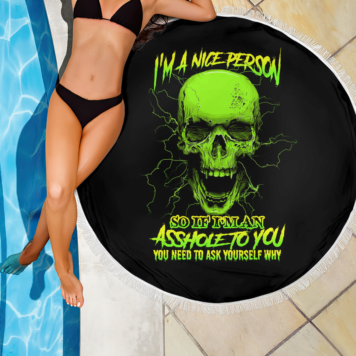 Round black beach blanket with neon green skull print and white fringe beside pool