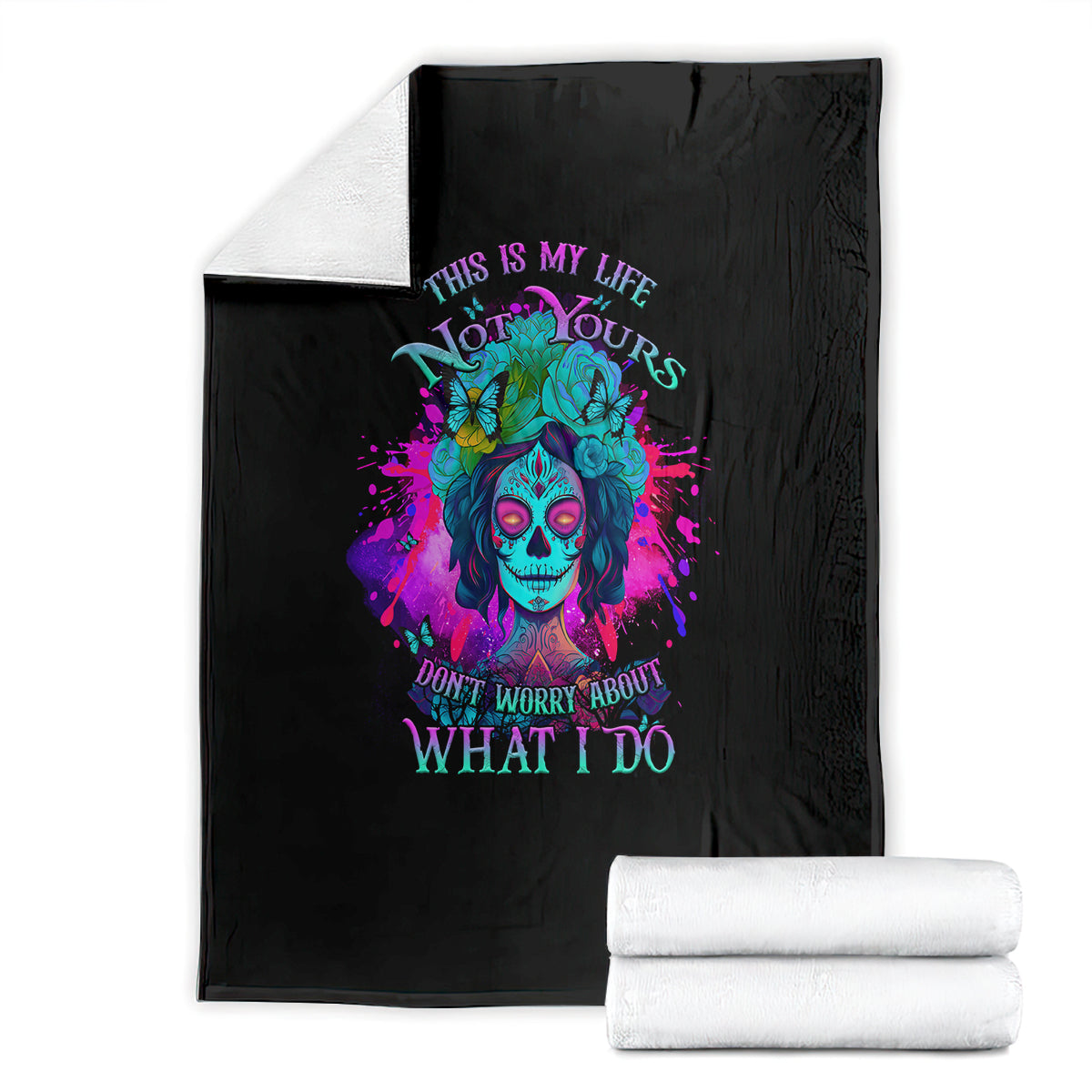 Black fleece blanket featuring colorful skull artwork and quote text, folded with white stacks.