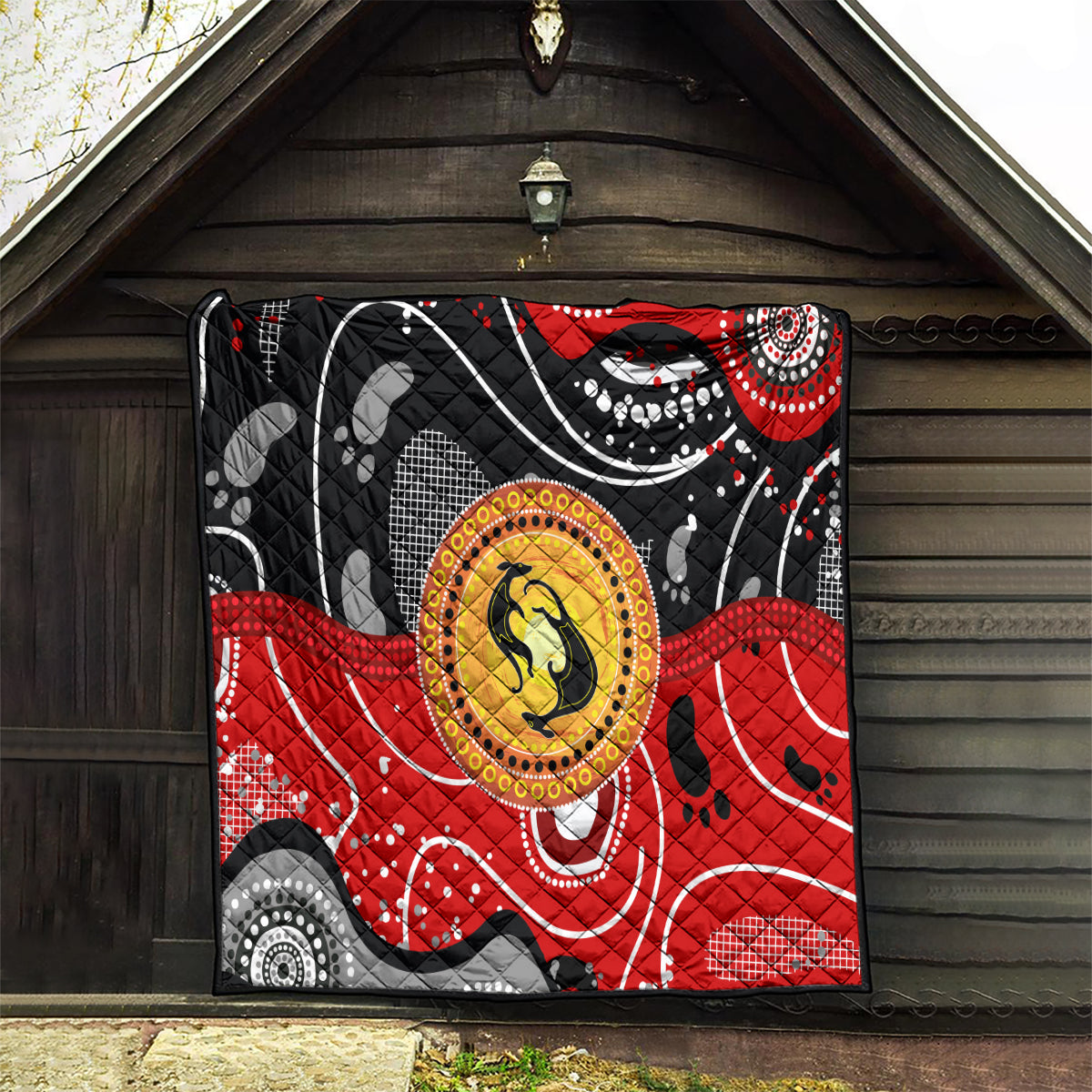 Multicolor quilt hanging outdoors with black base, red waves, and central kangaroo dot medallion