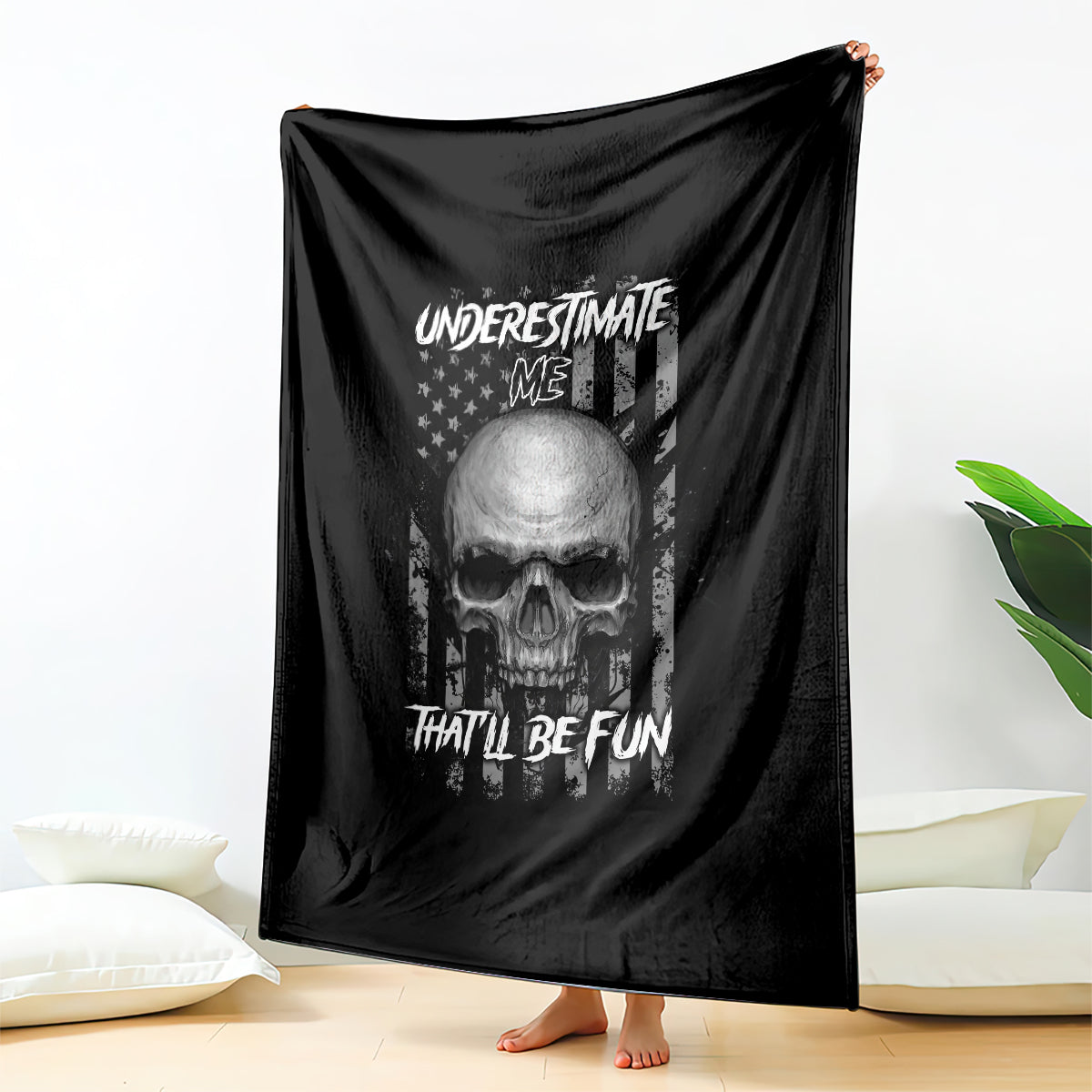 Black blanket with skull face and 'UNDERSTIMATE ME' text, draped over a bed