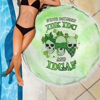 Round green beach blanket with skull faces graphic and fringed edge beside pool