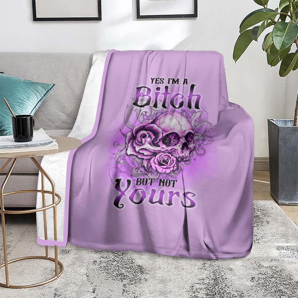 Purple throw blanket on a sofa with floral skull graphic and “YES I'M A Bitch BUT NOT Yours”.