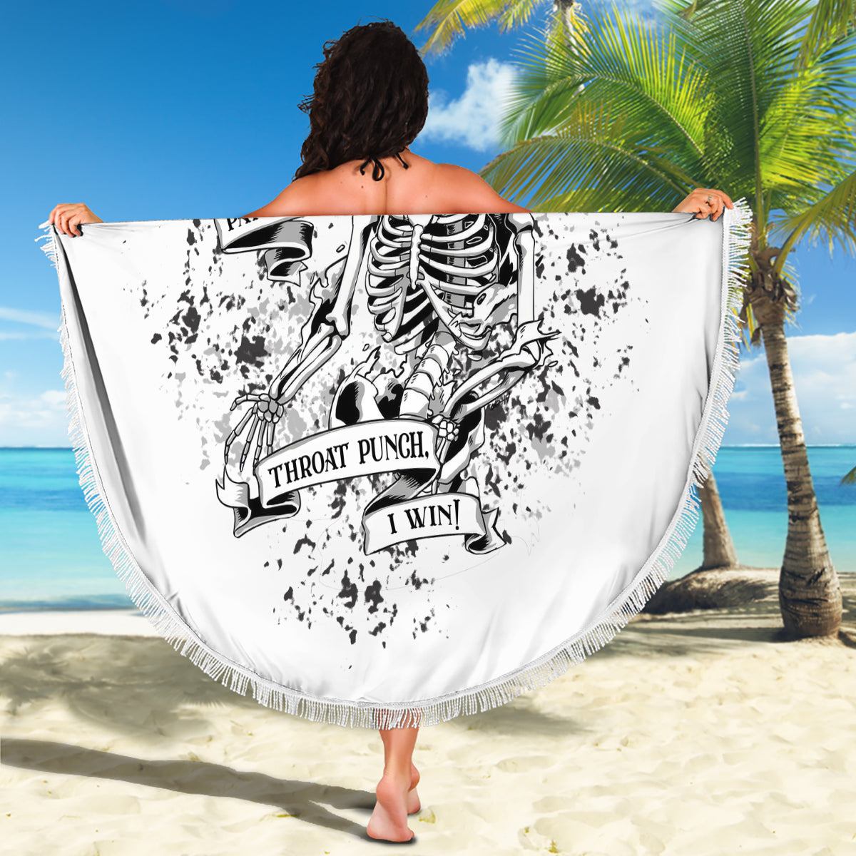 Round white beach blanket with black skull graphic and tassel fringe border, held up