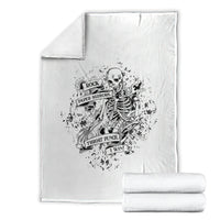 White throw blanket with black skeleton emblem; shown with two folded matching blankets