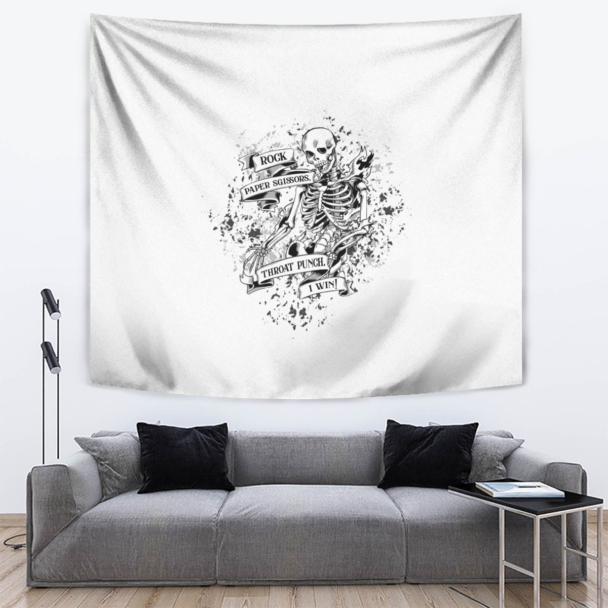 Black and white rock-paper-scissors skeleton skull tapestry over gray sofa.