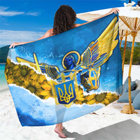 Blue and yellow sarong with trident emblem and sunflower graphic, draped on beach
