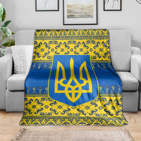 Blue and yellow ornate throw blanket with gold trident emblem, spread across gray couch