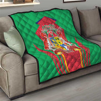 Green quilted blanket draped over gray sofa with central red crest shield emblem, diamond quilting.