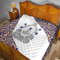 White quilt with blue border and central emblem motif, layered on a diamond quilted surface.
