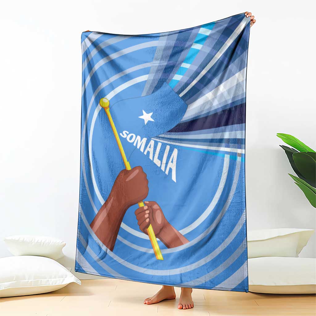 Blue Somalia flag blanket draped on floor with raised fist, spear icon, Somali text