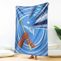 Blue Somalia flag blanket draped on floor with raised fist, spear icon, Somali text