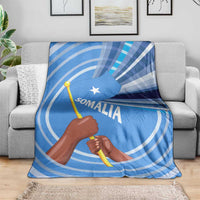 Blue Somalia flag blanket on gray sofa featuring raised fist and Somali wordmark