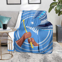 Blue Somalia flag blanket on armchair with raised fist and spear graphic, Somali text