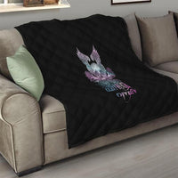Black quilt draped on couch with quilted diamonds and skull wings rose graphic on front.