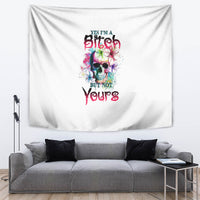 White tapestry with colorful skull and bold lettering, shown above a gray couch