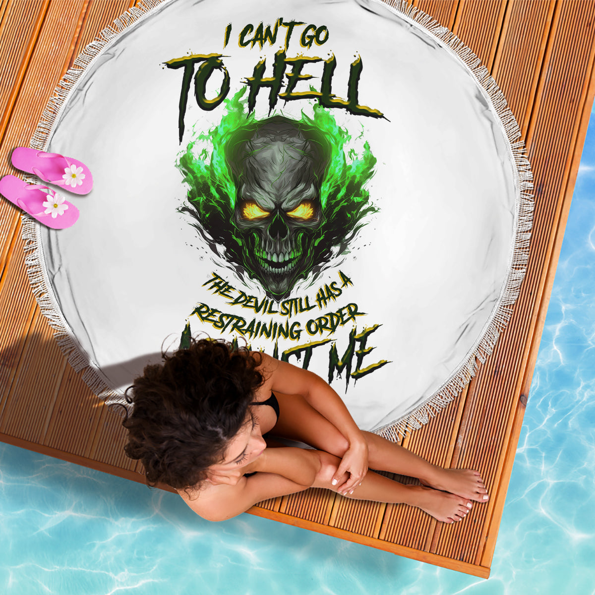 Round white beach blanket with green skull artwork and fringe border, on woven mat
