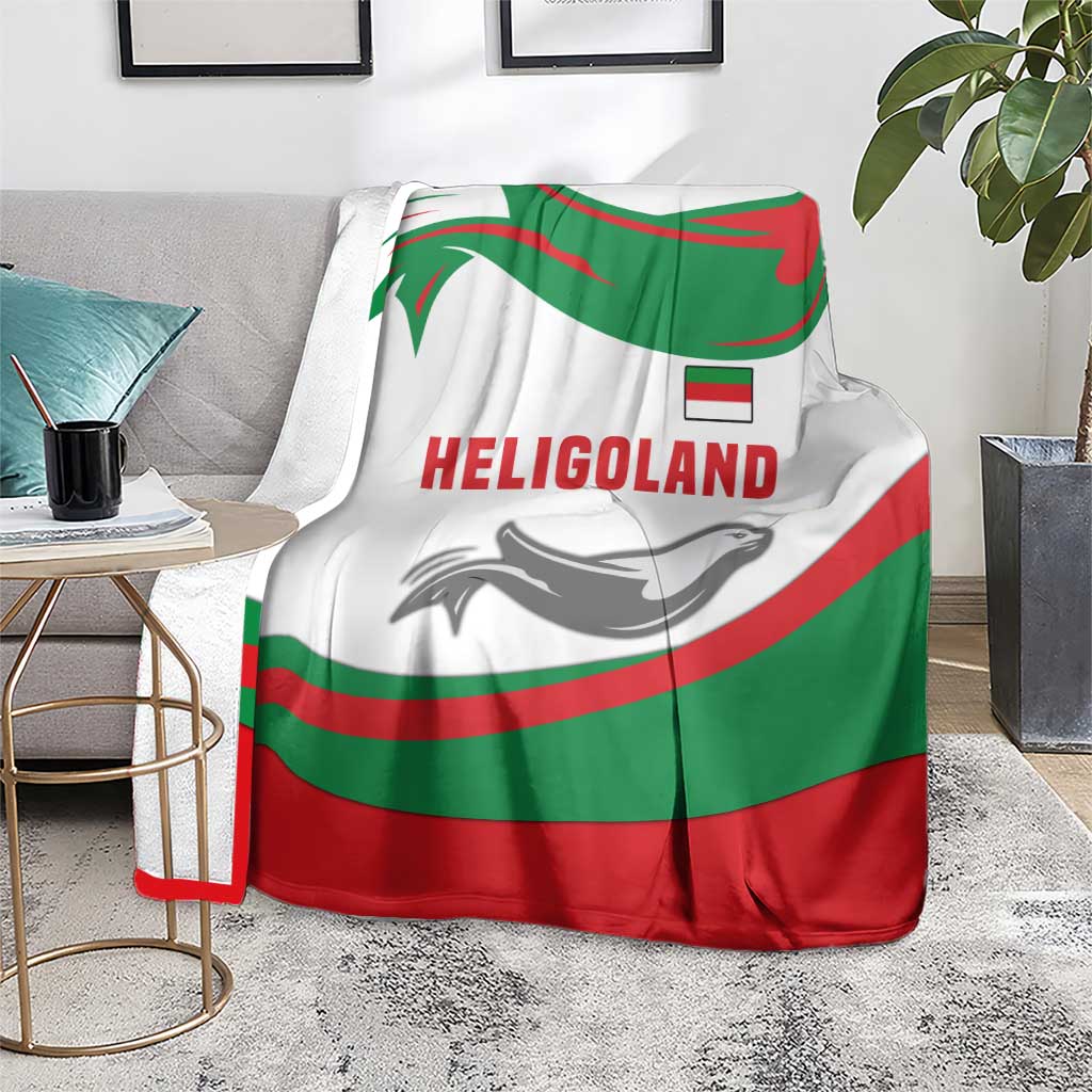 Green red white blanket with HELIGOLAND wordmark and seal graphic, draped on a couch