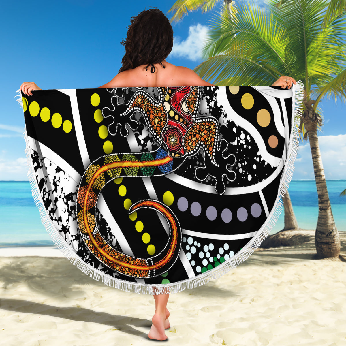 Fringed round beach blanket with multicolor lizard dot-art pattern held up on sand