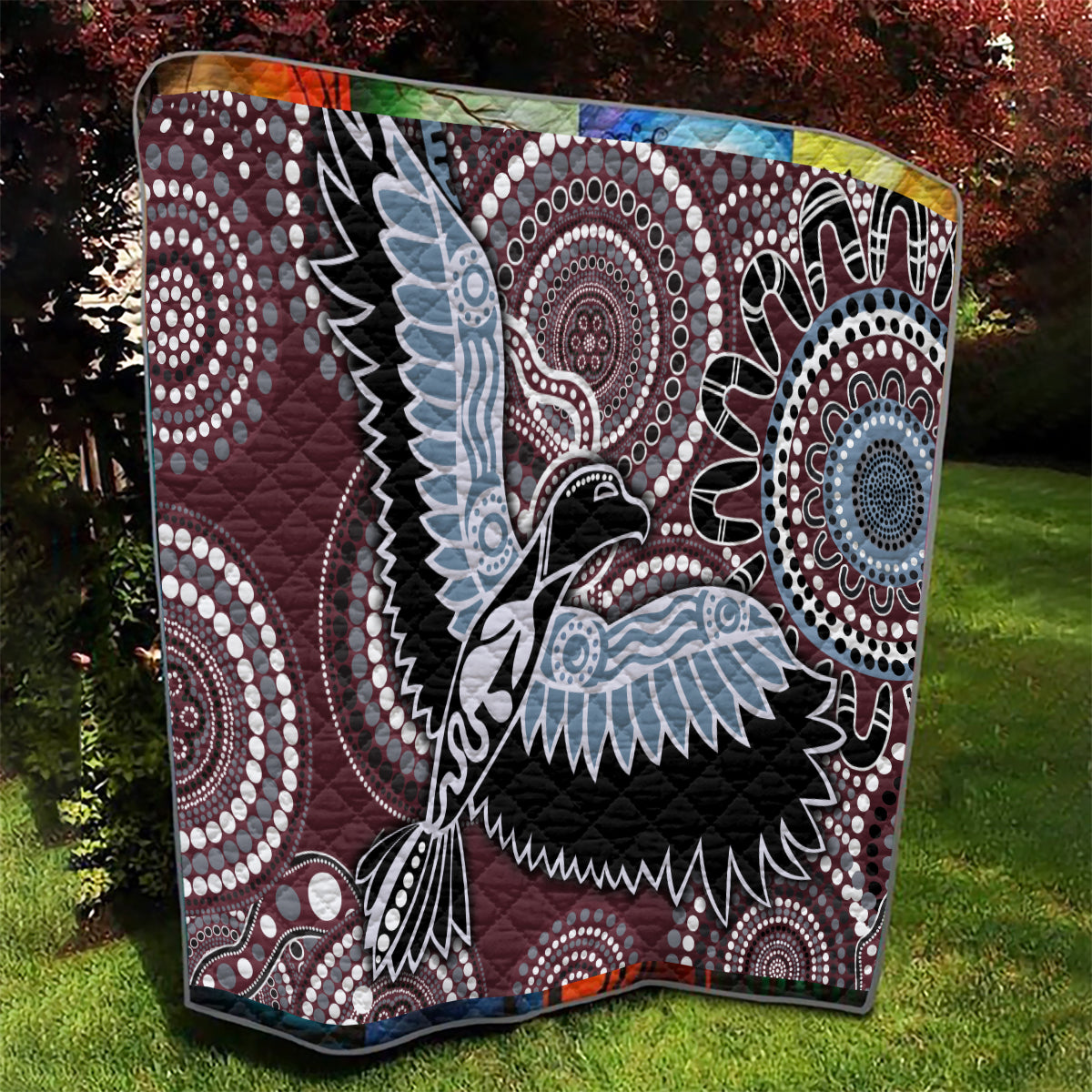 Burgundy Aboriginal bird quilt with swirling circular patterns in light blue, black and white