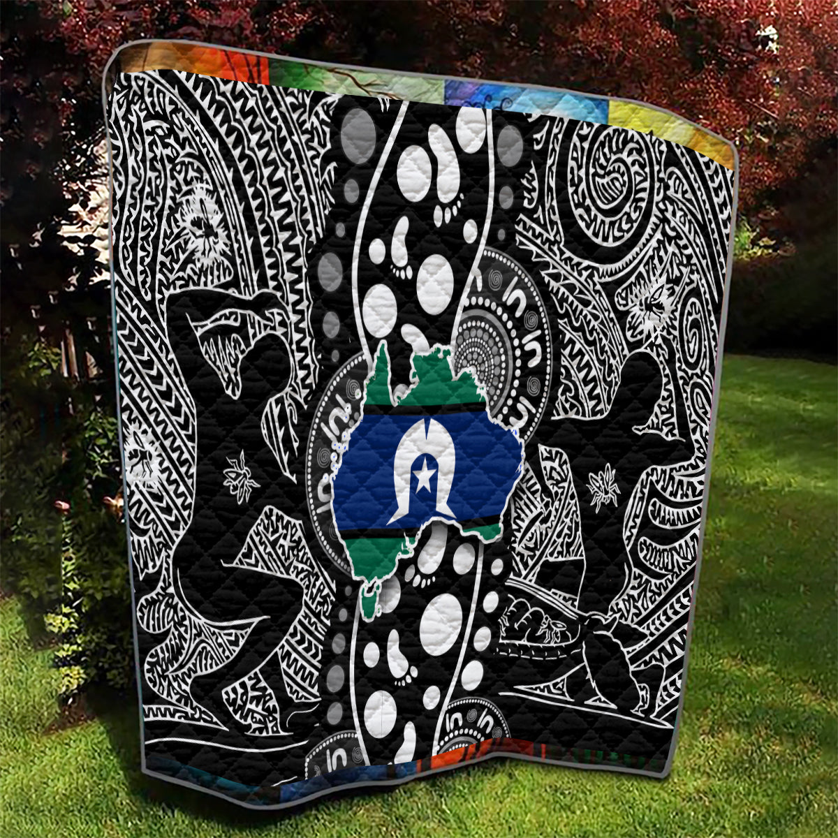 Aboriginal pattern quilt laid on lawn, black-and-white tribal designs with blue-and-green map