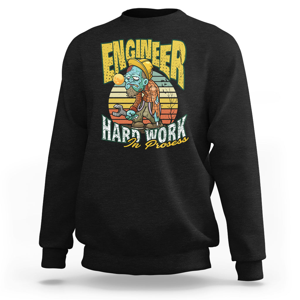 Black crewneck sweatshirt with front “Engineered Hard Work In Progress” graphic