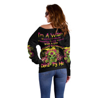 Off-shoulder black sweater with multicolor skull graphic and slogan on back