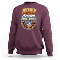 Maroon crewneck sweatshirt with colorful “Caretaker” miracle worker graphic