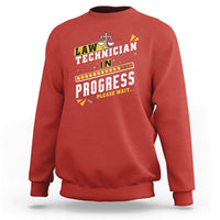 Red crewneck sweatshirt with filmstrip "In Progress" graphic and scales icon