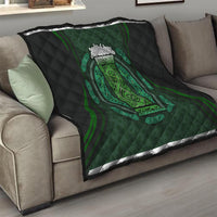 Black quilt blanket on couch with green Celtic oval crest, quilted diamond stitching along edges