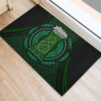 Rectangular black rubber doormat with centered green Celtic emblem, corner view