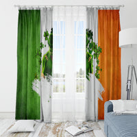 Hanging window curtains with green, gray, and orange clover print on a curtain rod