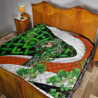 Multicolor quilt on bed with central white cross, green shamrock pattern, and orange edges