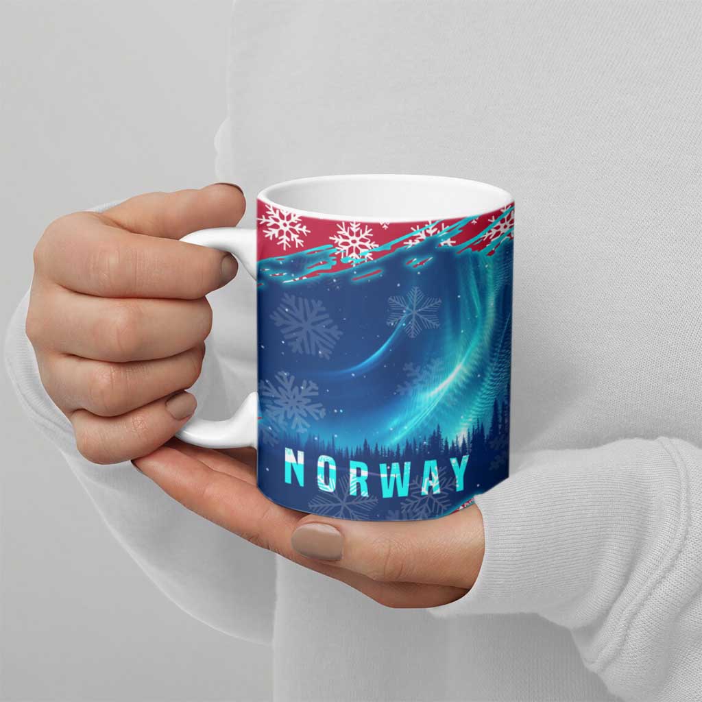Blue ceramic mug with NORWAY text, northern lights, and snowflake pattern, held