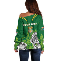 Green off-shoulder sweater back with placeholder text, crest badge, protea and flag