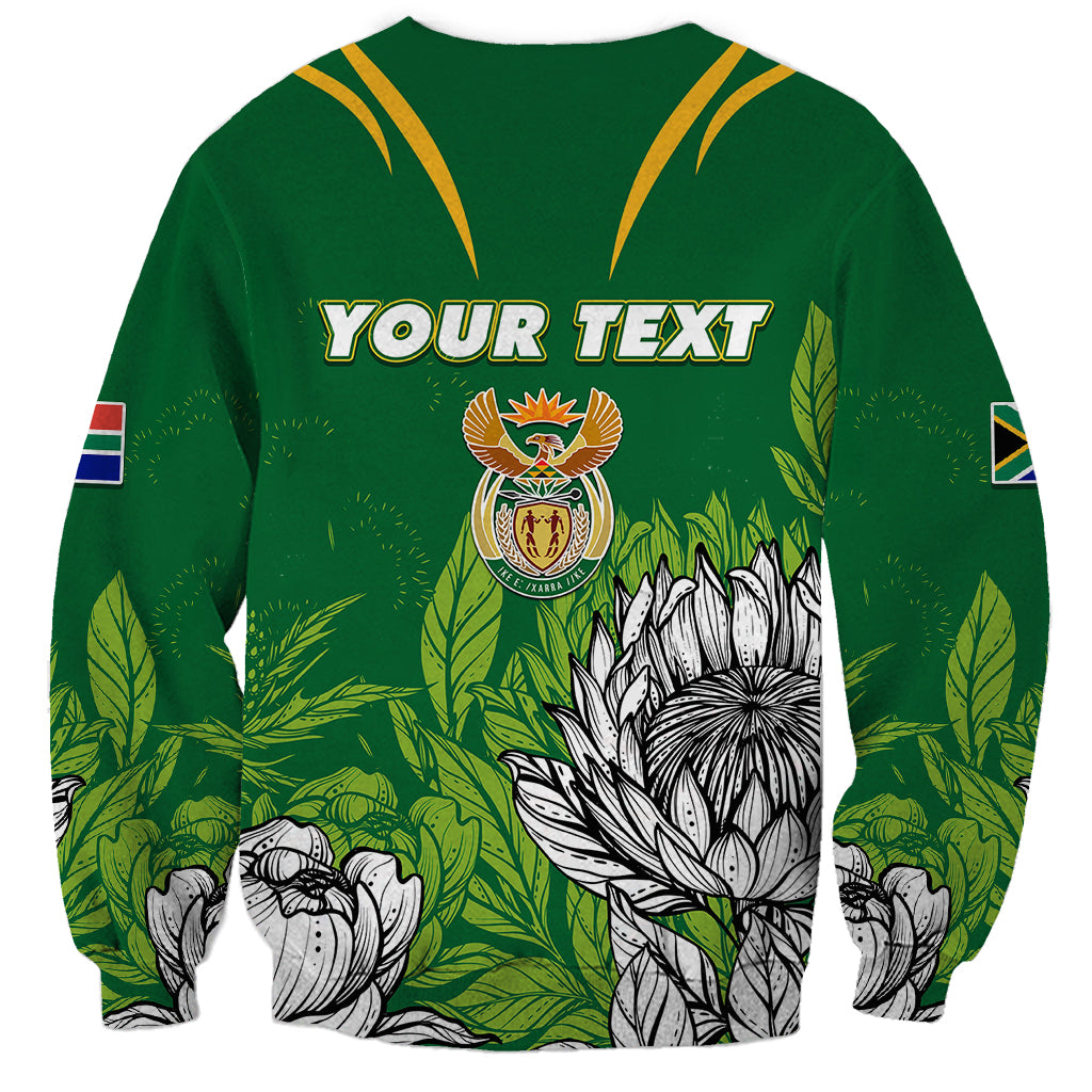Green sweatshirt with yellow V yoke, Your Text print, crest and protea flowers, sleeve flag patches