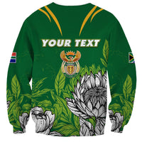 Green sweatshirt with yellow V yoke, Your Text print, crest and protea flowers, sleeve flag patches