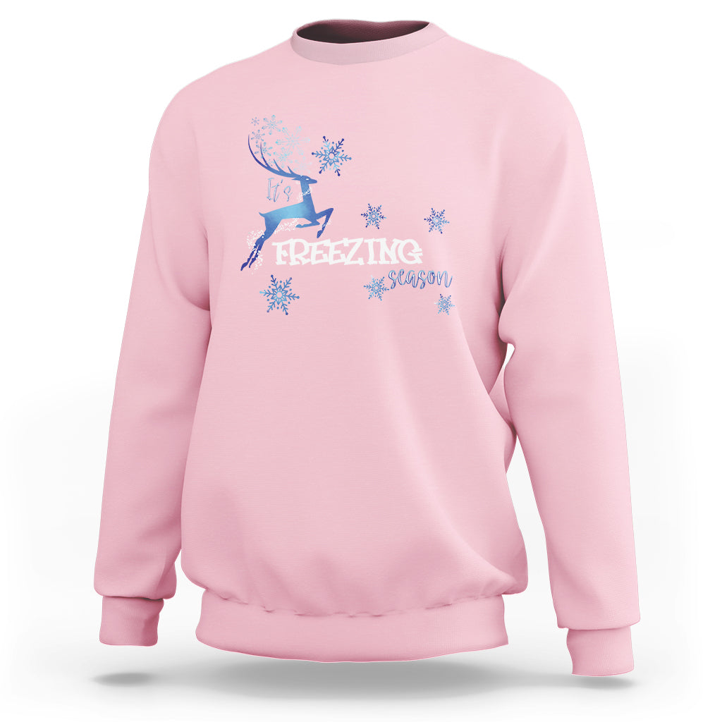 Light pink crewneck sweatshirt with blue reindeer and snowflake graphic, “Freezing Season”