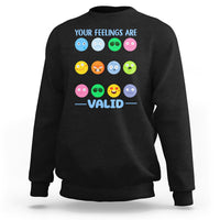 Black sweatshirt with “YOUR FEELINGS ARE VALID” text and colorful emotion-face graphics.