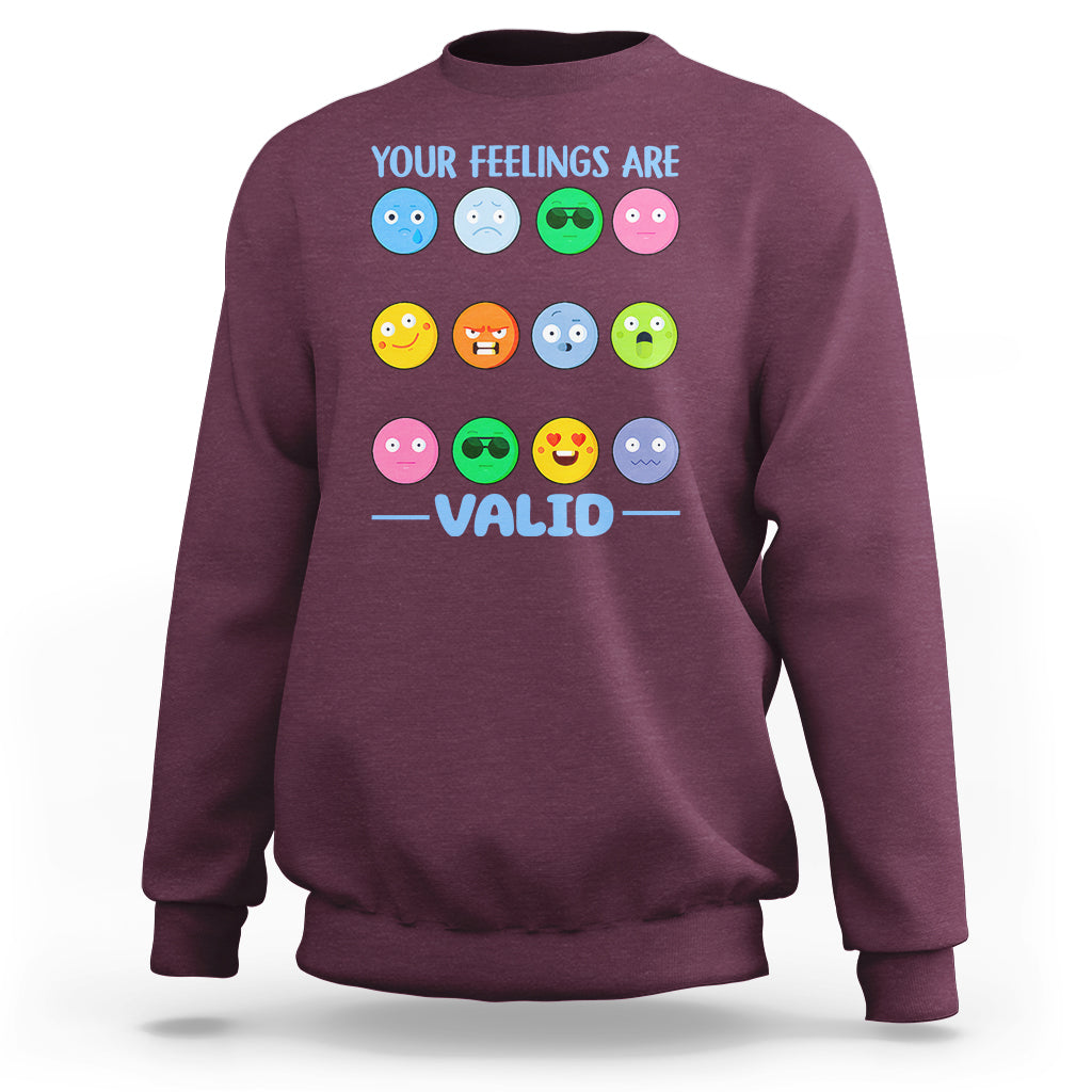 Maroon sweatshirt with “YOUR FEELINGS ARE VALID” text and colorful emotion-face graphics.