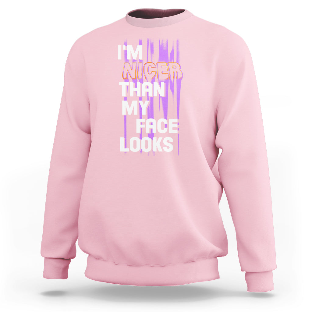 Light pink crewneck sweatshirt with front graphic text: “I’m nicer than my face looks”