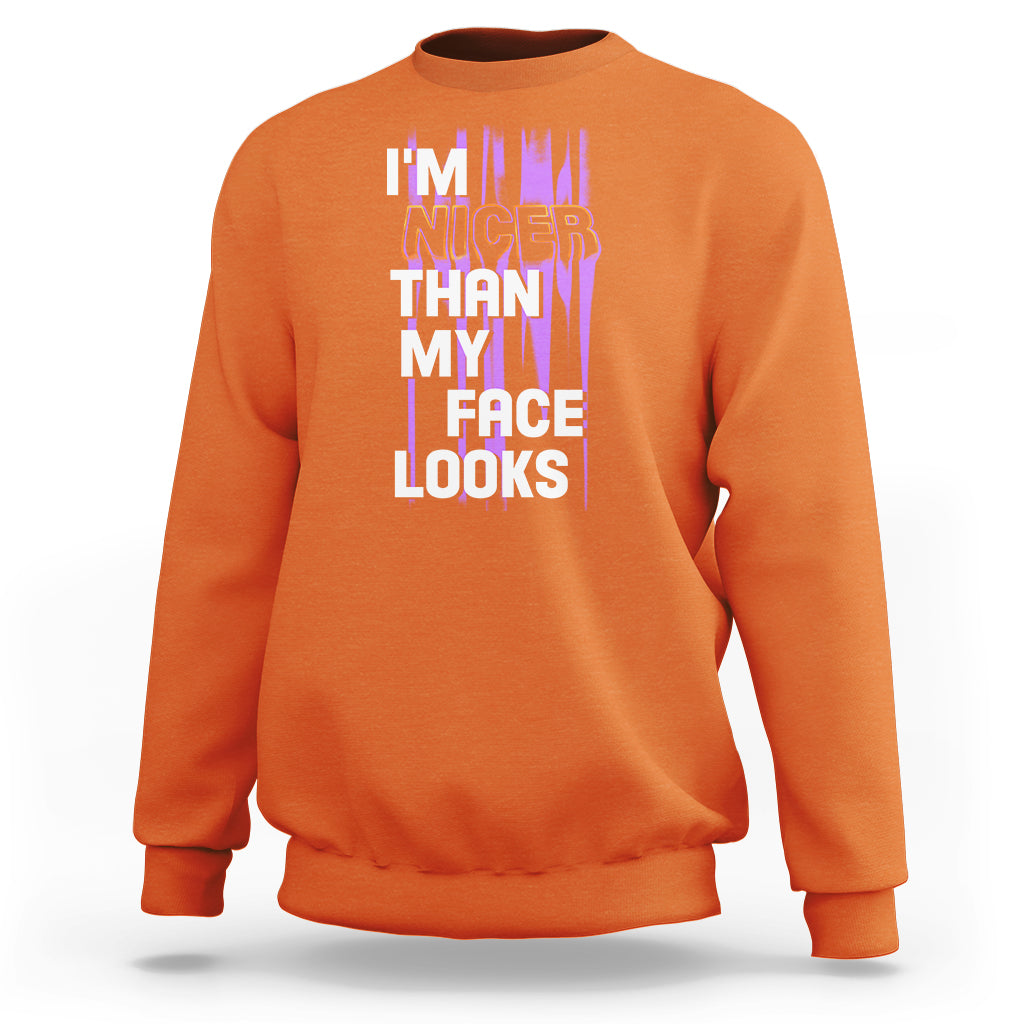 Orange crewneck sweatshirt with front graphic text: “I’m nicer than my face looks”