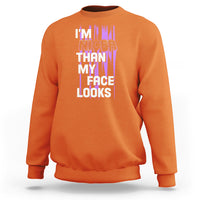 Orange crewneck sweatshirt with front graphic text: “I’m nicer than my face looks”