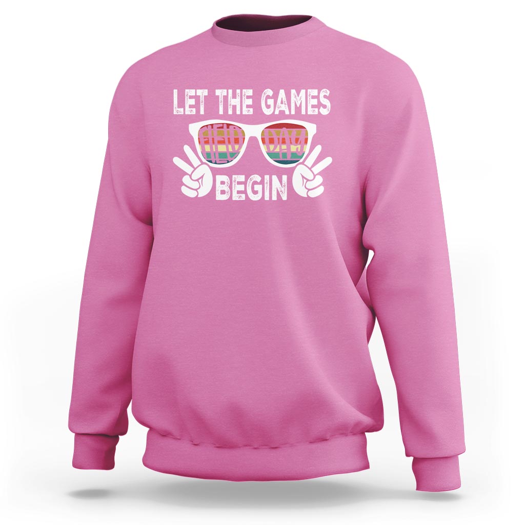 Pink sweatshirt with “LET THE GAMES BEGIN” graphic and sunglasses hands