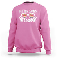 Pink sweatshirt with “LET THE GAMES BEGIN” graphic and sunglasses hands