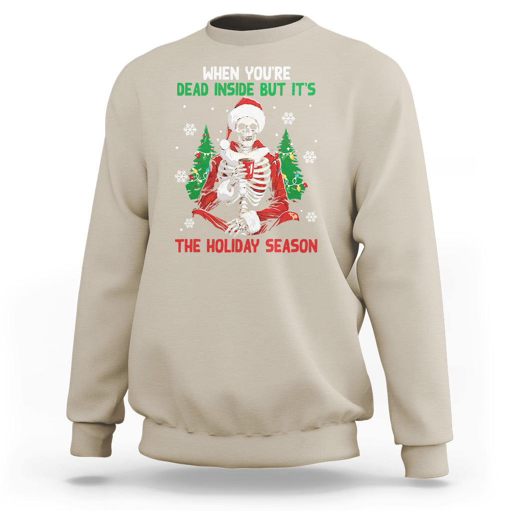 Sand color crewneck sweatshirt with cartoon skeleton in Santa hat and "THE HOLIDAY SEASON" print