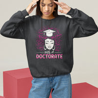Black crewneck sweatshirt with queen graduation graphic and "With a DOCTORATE" text.