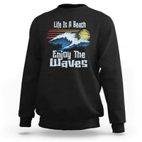 Black crewneck sweatshirt with beach wave graphic and “Enjoy The Waves” text